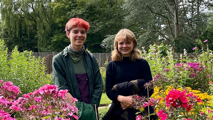Die beiden FÖJ-lerinnen des Botanischen Gartens stehen in einem pinkblühenden Blumenbeet