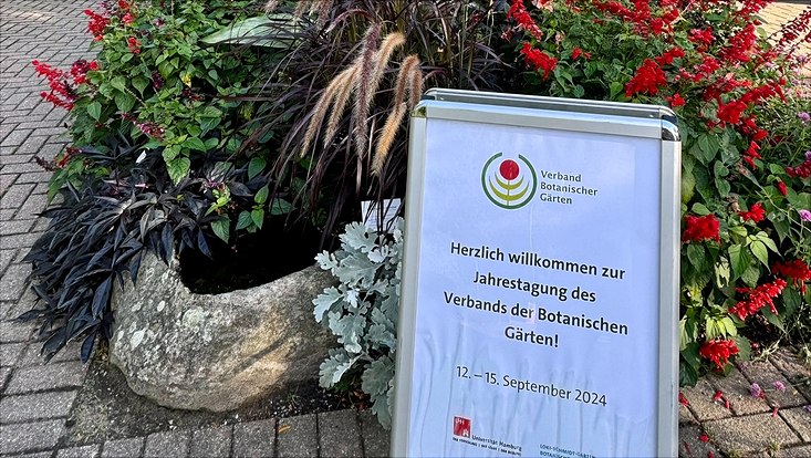 Eingang des Botansichen Gartens mit angeschnittenem Poster von der Verbandstagung der Botanischen Gärten 2024