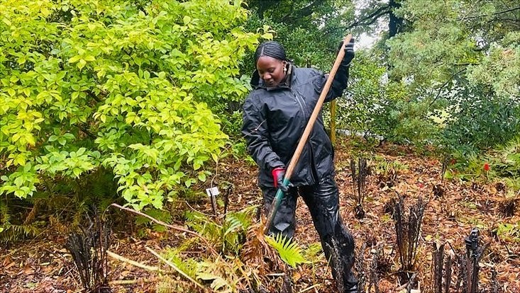 Die Gärtnerin Liberta steht in einer Wiese und harkt