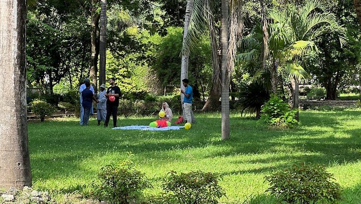 Blick auf eine grüne Wiese, umstanden mit Palmen. Einige Menschen sitzen auf der Wiese. Botanischer Garten Daressalam