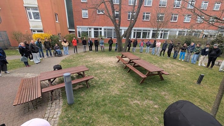 Foto von der 4. Seminarwoche. Viele junge Menschen stehen im Halbkreis auf einer Wiese