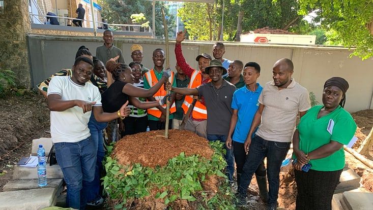 Mitarbeitende des Botanischen Gartens in Dar es Salaam stehen im Halbkreis um einen Baumstumpf herum